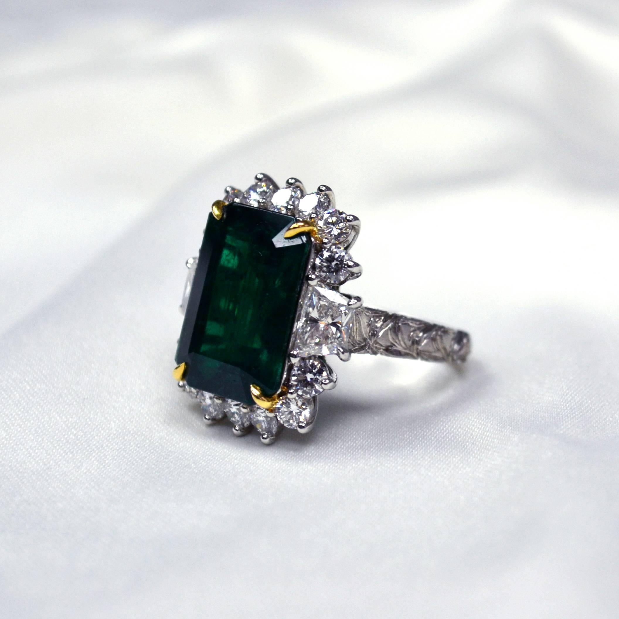 Ring in platinum set with an intense green emerald cut Zambian Emerald (7.78 carat), 2 trapezoid cut Diamonds (1.43 carats) and 14 round brilliant-cut Diamonds (1.36 carats).

Featuring beautifully carved shank.
Ring US Size 6.
*Complimentary