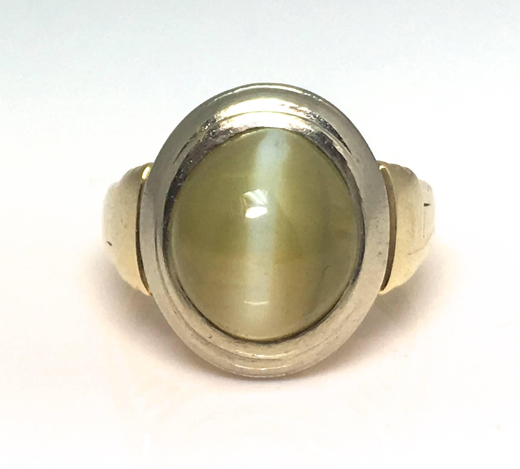 A Circa 1960s Chrysoberl Cats Eye Mans ring. This cabochon cut Cats eye is in a rub over set surrounded by 18ct white gold to a yellow gold shank. The stone weighs circa 8 carats. The beautiful and unusual attribute or phenomenon of this stone is