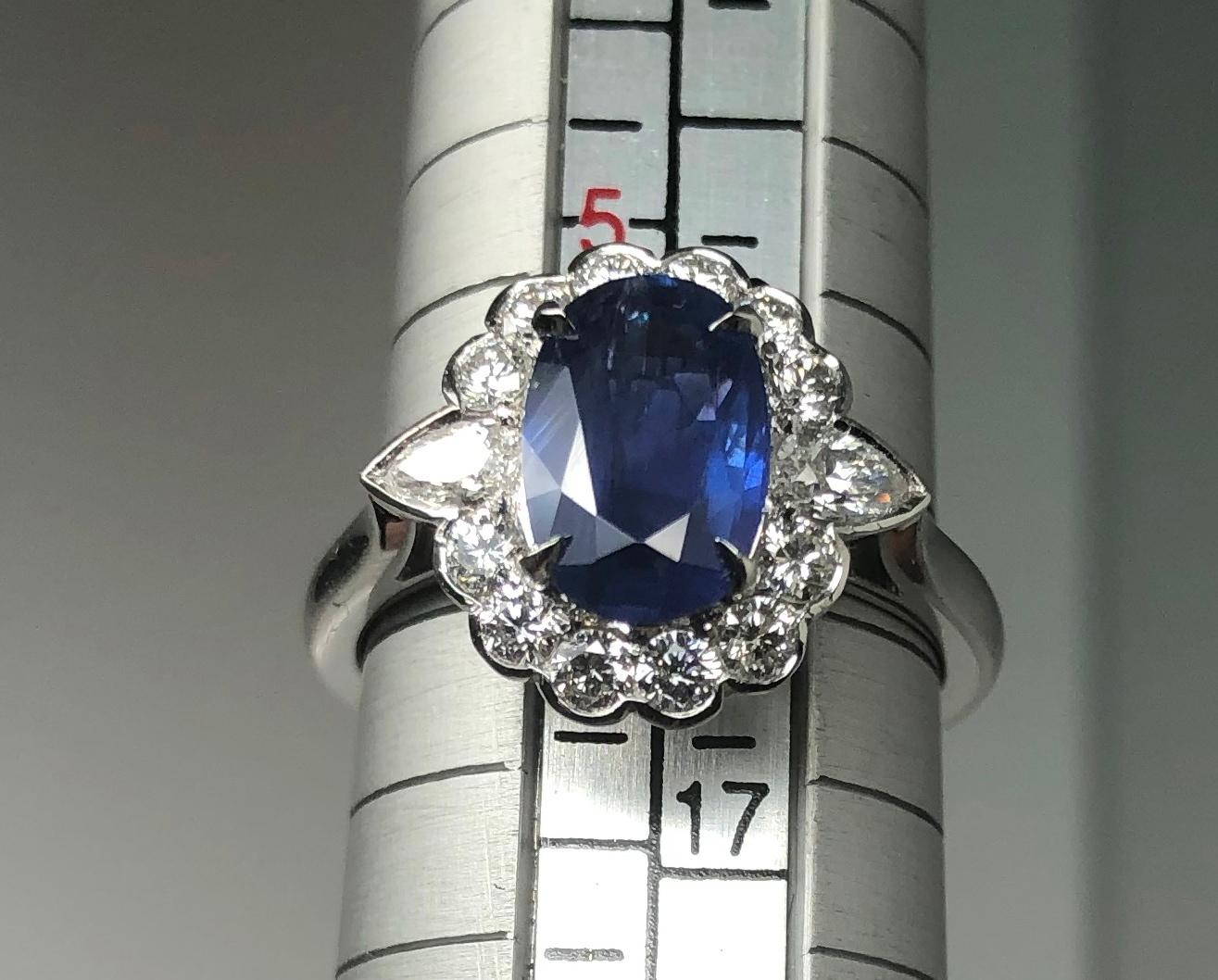 A Sapphire weighing 1.85 carats set in a diamond cluster ring flanked by two pear shape diamonds. The stone is mounted in Platinum. The stone in our opinion is a Royal blue colour with a small inclusion only visible in a certain angle. This is