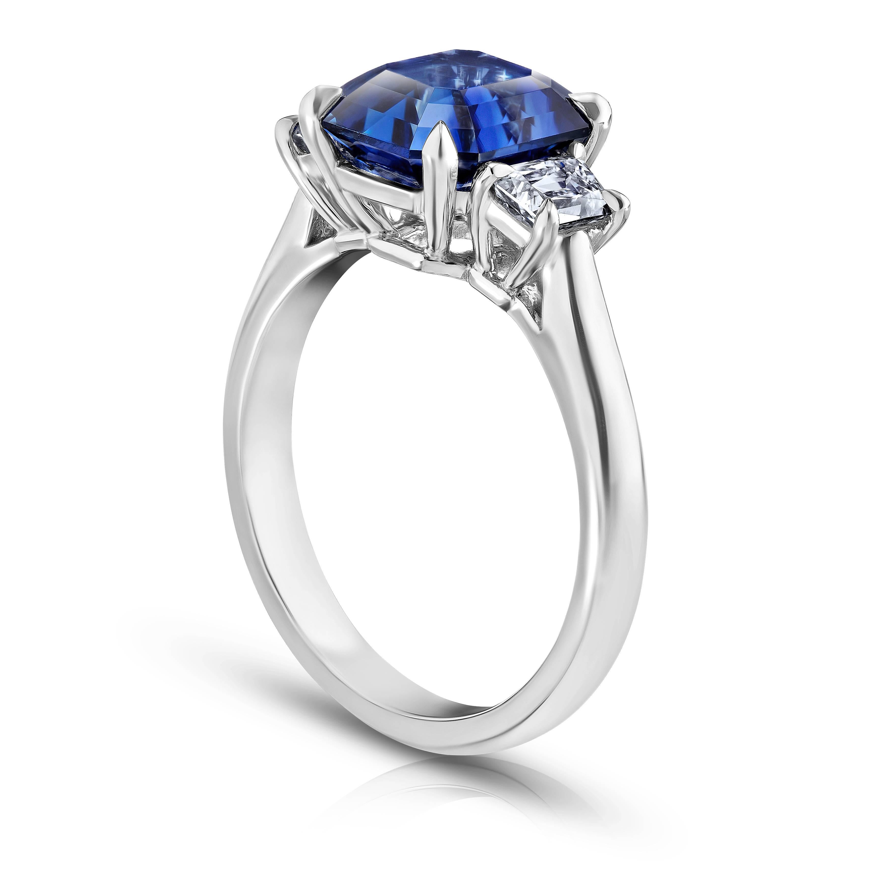 This blue sapphire ring is impeccable. Its center stone is a  emerald cut "cornflour blue" sapphire weighing 3.86 carats. The stone is perfectly cut and extremely clean with great  color saturation. Two trapezoid cut diamonds weighing .62