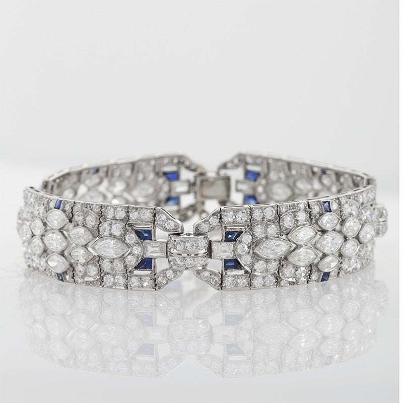 An American Art Deco platinum bracelet with diamonds. The 4 section flexible bracelet is set with Old European-cut round and marquise-cut diamonds with an approximate total weight of 12.30 carats. The bracelet has 24 calibe cut sapphire accents with