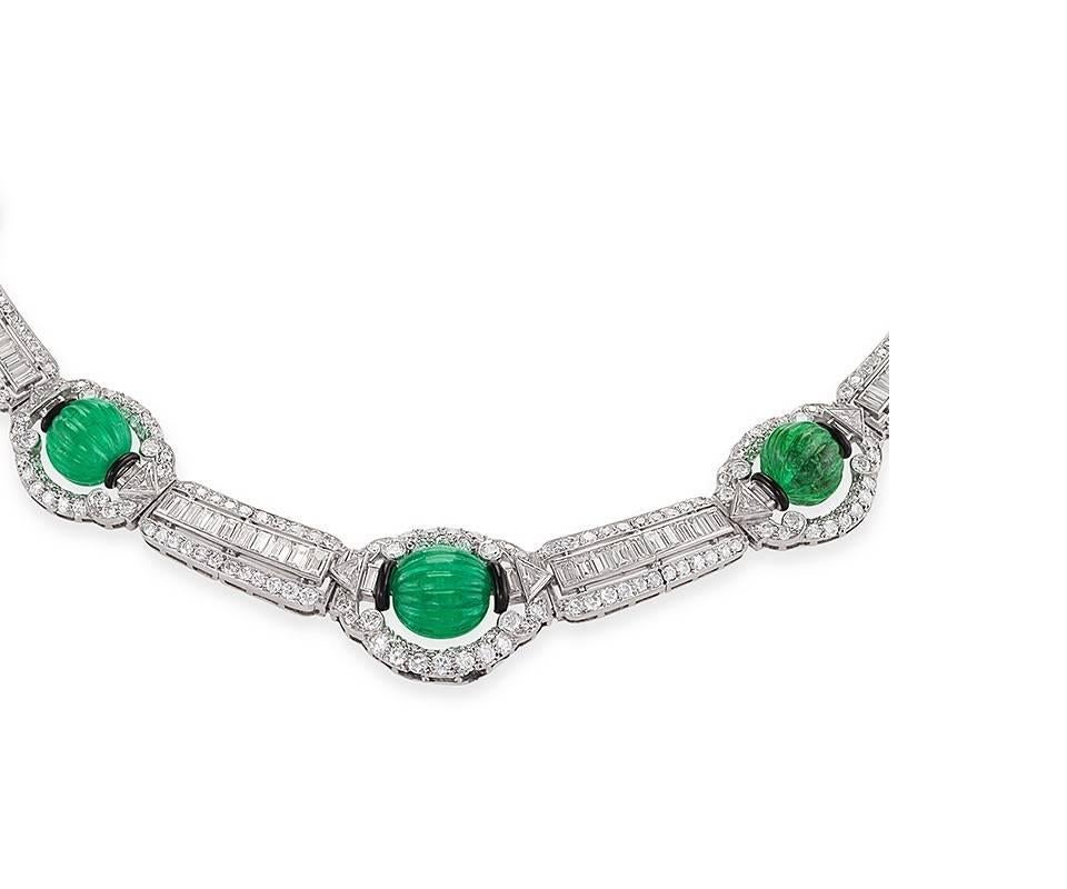 Dating from the 1930s, this Art Deco platinum necklace, composed of nineteen carats of carved emeralds and over eleven carats of diamonds, is an artistic period jewel with a striking visual aesthetic. Centering on five graduating melon-carved