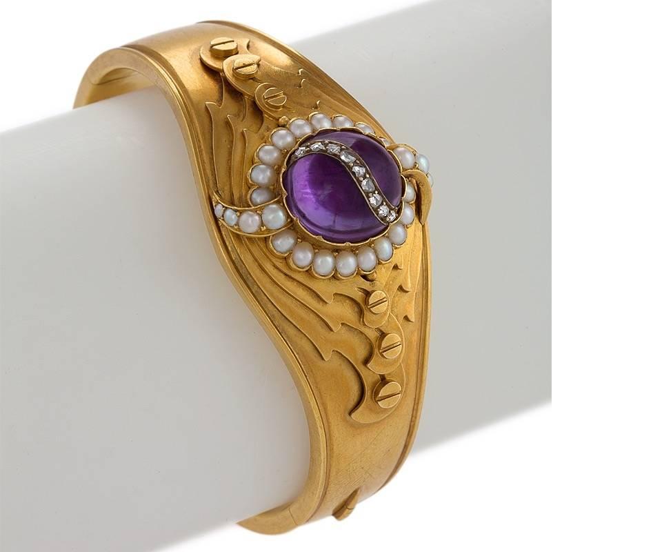 An English Victorian 18 karat gold bangle bracelet with amethyst, diamonds and pearls. The hinged bangle bracelet centers on a cabochon amethyst with a ribbon of 9 rose-cut diamonds with an approximate total weight of .26 carat. The center cluster
