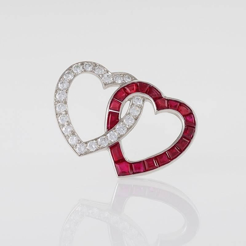 An American platinum brooch with diamonds and rubies by Oscar Heyman. The double heart brooch has 21 round-cut diamonds with an approximate total weight of .65 carat, and 18 calibre-cut rubies with an approximate total weight of 1.40 carats. Circa
