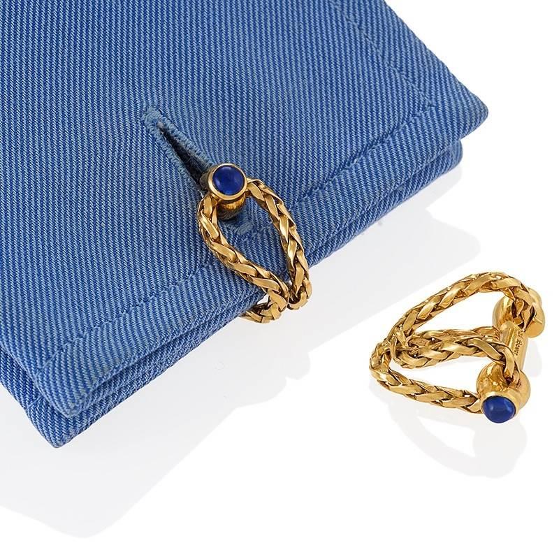 A pair of French Mid-20th Century 18 karat gold cuff links with sapphires by Boucheron. The cuff links have 4 cabochon sapphires with an approximate total weight of .40 carats. The stirrup cuff links are formed with 2 strands of flexible woven