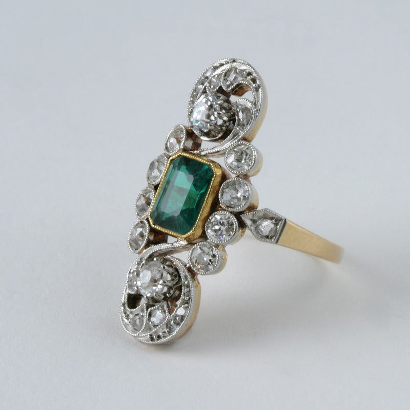 An English Edwardian 18 karat gold and platinum ring with emerald and diamonds. The ring has an emerald-cut emerald with an approximate total weight of .90 carat in a gold bezel setting, and 2 milegrain set old European-cut diamonds with an