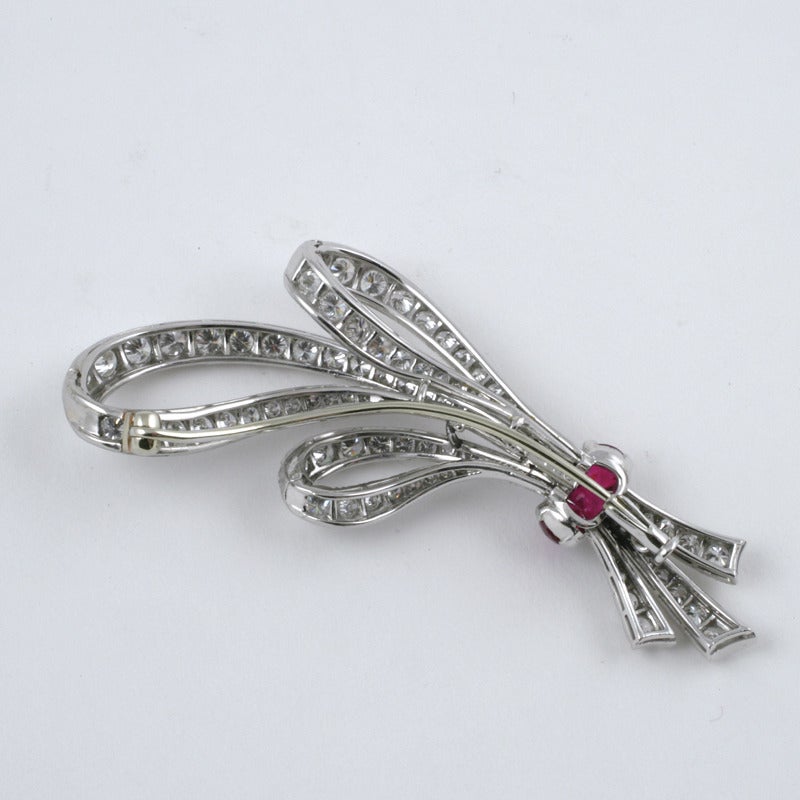 A Mid-20th Century platinum brooch with diamonds and rubies. The brooch has 98 round-cut diamonds with an approximate total weight of 5.35 carats, G/H color, VS clarity, and 3 round-cut rubies with an approximate total weight of .50 carats. The