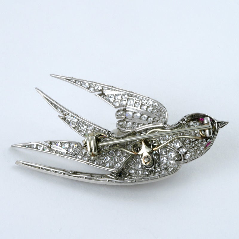 A French Art Deco platinum and enamel brooch with diamonds and rubies. The brooch has 306 round diamonds with an approximate total weight of 8.75 carats, and 2 cabochon ruby accents.  Circa Late 1930’s.

This dimensional brooch representing a dove