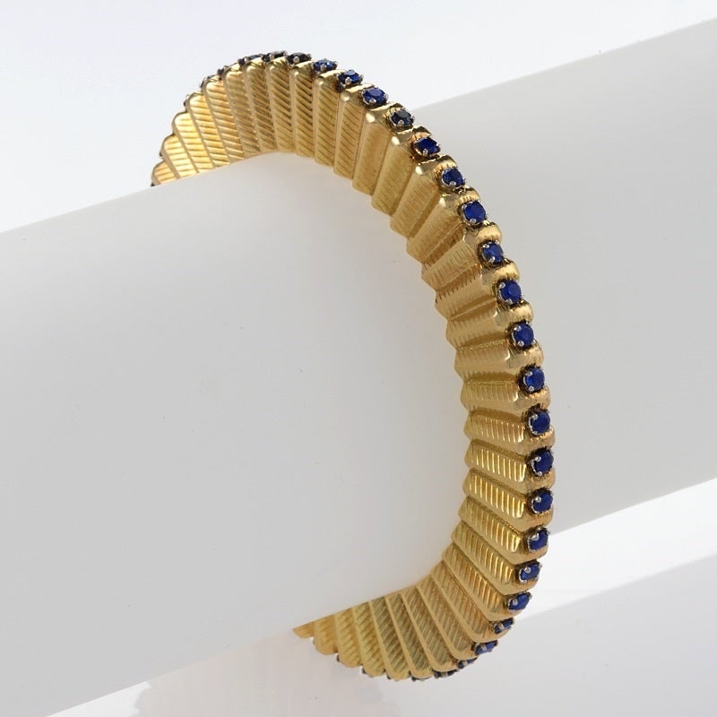 A French 18 karat gold bangle bracelet with sapphire by Cartier. The form of this bracelet refers to gears and is a classic :Machine Age” design.  The bangle bracelet has 48 round sapphires with an approximate total weight of 4.80 carats.  
Circa