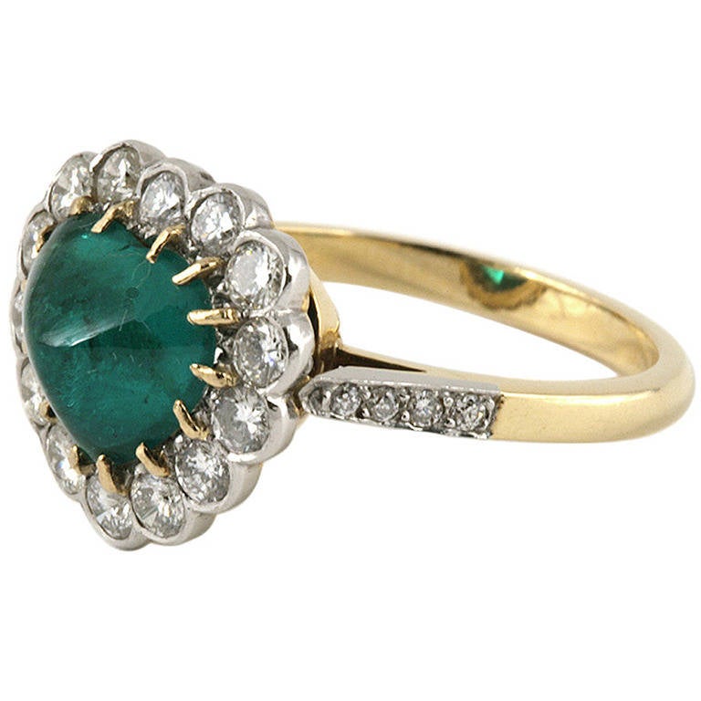 A French 18 karat gold and platinum ring with emerald and diamonds. The center heart-shaped cabochon emerald, with an approximate total weight of 2.80 carats, is surrounded by 14 round-cut diamonds with an approximate total weight of .70 carat.