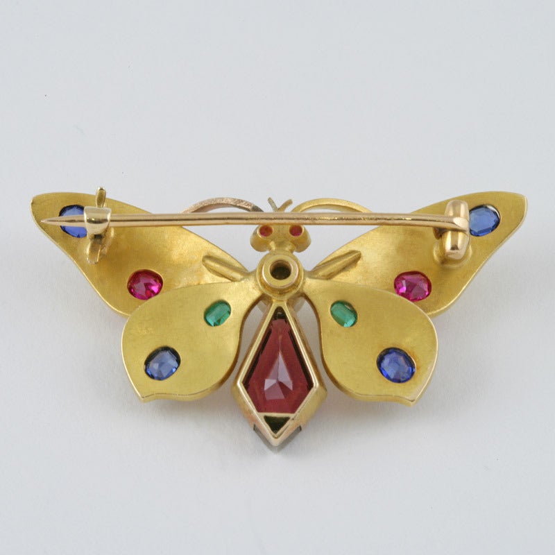An Austrian Art Nouveau 18 karat gold brooch with diamond, sapphires, rubies, emerald, garnet and pearl. The bloomed gold, three  dimensional butterfly is set with 1 fancy cut garnet approximately 1.40 carats, 1 diamond  approximately .03 cts, 4