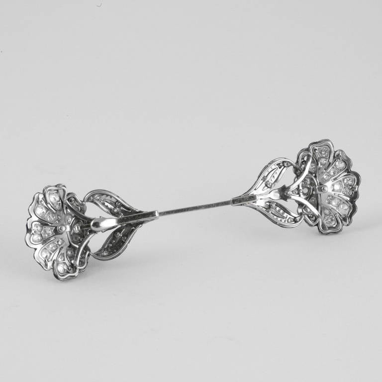 A French Art Deco platinum, diamond and enamel jabot pin that features two flowers on each end that are decorated with 100 old European cut diamonds and black enamel that form two flowers. The diamonds have an approximate total weight of 2.90