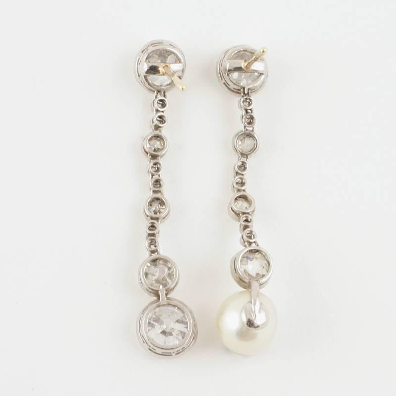 A pair of Art Deco platinum articulated earrings with natural pearl and diamonds. The miligrain bezel set earrings have 3 old European-cut diamonds with approximate total weights of 1.60, 1.00, and .95 carats, and 2 old European-cut diamonds