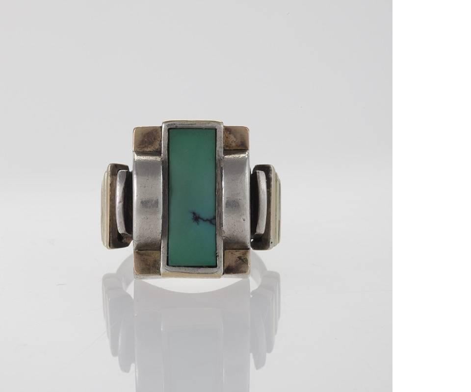 A French Art Deco silver and 18 karat gold ring with turquoise by Jean Després. The ring has a bezel set rectangular-cut turquoise stone with dimensional arched side elements and gold steps on the shoulders. Hand engraved signature.  Circa 1930's.