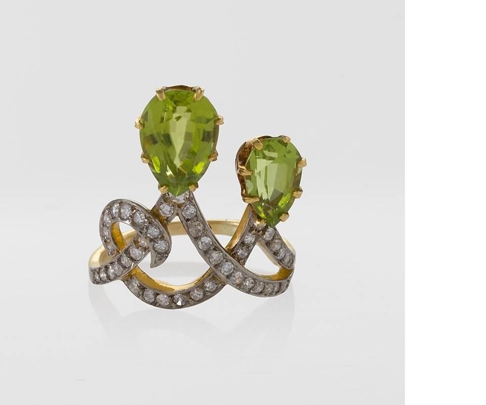 A French Early 20th Century 18 karat gold and platinum ring with peridots and diamonds attributed to Maison Péconnet. The ring features 2 marquise-cut peridots with an approximate total weight of 2.55 and 1.25 carats respectively, and 42 round
