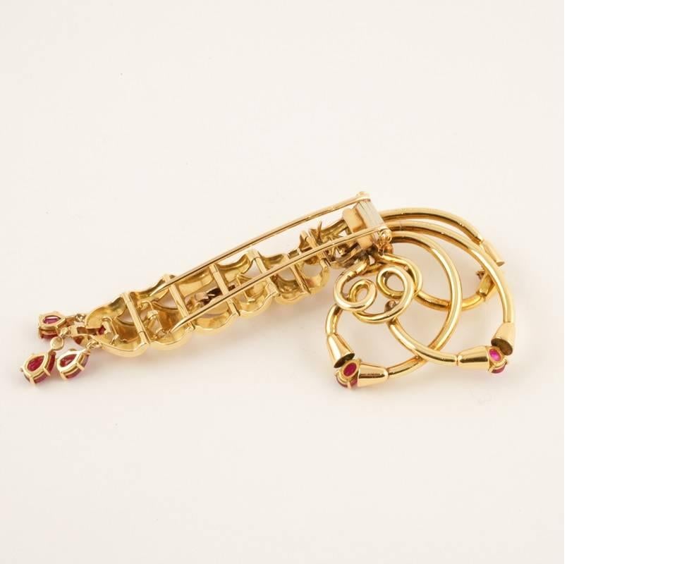 French Retro gold and ruby brooch by Mellerio. This 18-karat gold brooch features a graduated tank chain accented with calibré-cut rubies topped with gold spirals bearing oval-cut rubies. Three pear-cut rubies dangle off the bottom. Altogether, the