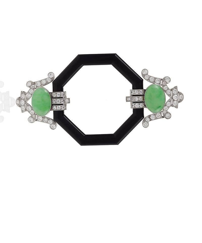 A French Art Deco platinum brooch with diamonds, jadeite jade and onyx. The brooch has 60 old European-cut diamonds with an approximate total weight of 3.50 carats, surrounding 2 cabochon jadeite jade stones which flank an onyx octagonal center.  