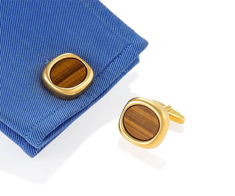A pair of English Mid-20th Century 18 karat gold cuff links with tiger eye by Sannit & Stein. The cuff links have polished tiger eye, bezel set in a cushion shape.  Wing backs. 

Sannit & Stein were fine jewelry makers in London who made