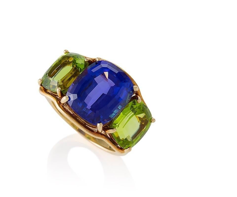 An Estate American 18 karat gold ring with tanzanite and peridots by Verdura. The ‘Three Stone’ ring has a cushion-cut tanzanite with an approximate  weight of 8.00 carats, flanked by 2 cushion-cut peridots with an approximate total weight of 6.40