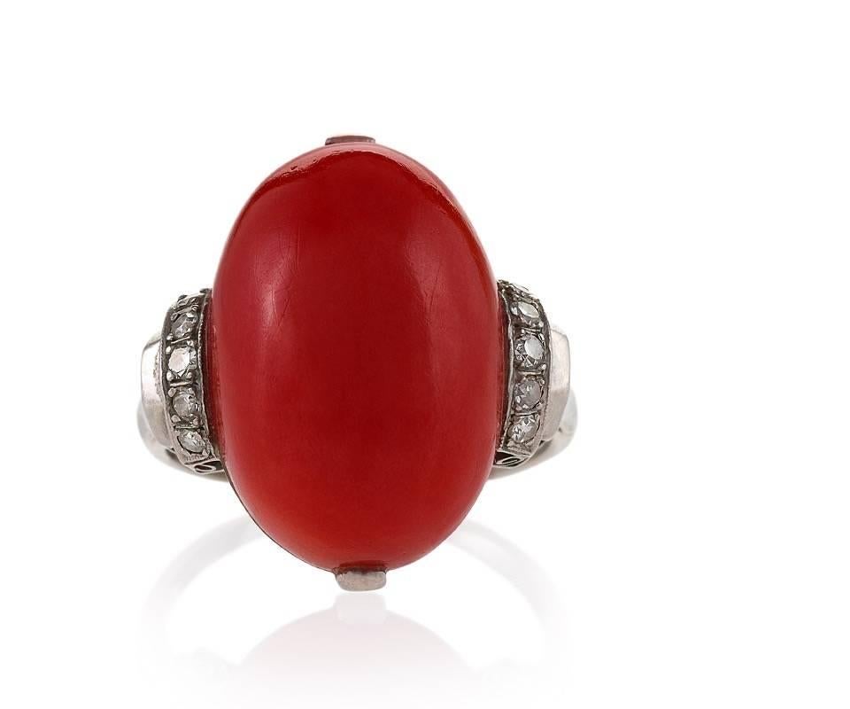 A French Art Deco platinum ring with diamonds and red coral. The ring has a red coral cabochon and 20 old European-cut diamonds with an approximate total weight of .20 carat.  The ring is composed of diamond-set step shoulders, and a deeply scrolled