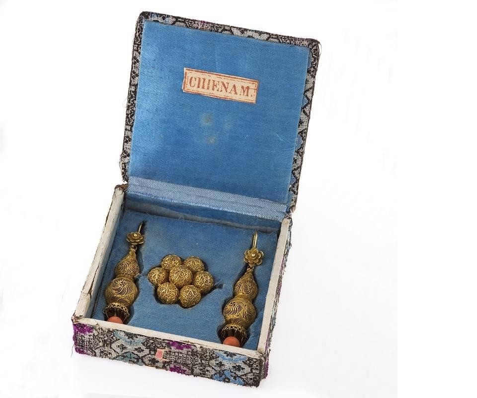 An Antique Chinese 18 karat gold earring/ brooch suite with coral. The earrings have 2 coral beads measuring 7.03-7.02 mm. and are composed of two graduated filigree and woven balls from which the articulated coral and gold fringe hangs. The