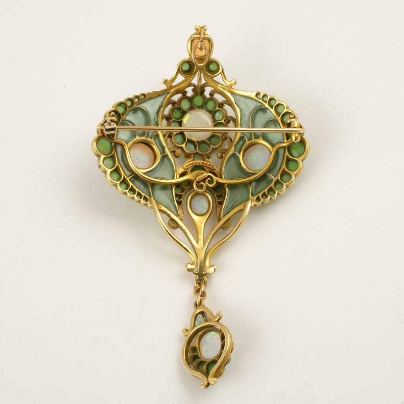 An American Art Nouveau 18 karat gold and enamel pendant brooch with opals and chrysoprase by Marcus & Co.. The pendant brooch has 6 cabochon white opals, 63 cabochon chrysoprase stones and plique-à-jour enamel. Suspended from the brooch is an opal