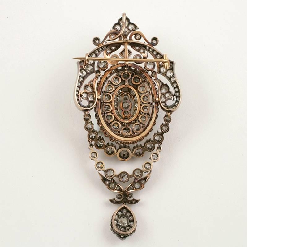 This extraordinary French silver-topped gold pendant brooch, from the era of Napoleon III, is designed with scrolling floral motifs suspending articulated double festoons, all set with over twelve carats of old mine-cut diamonds that drop and