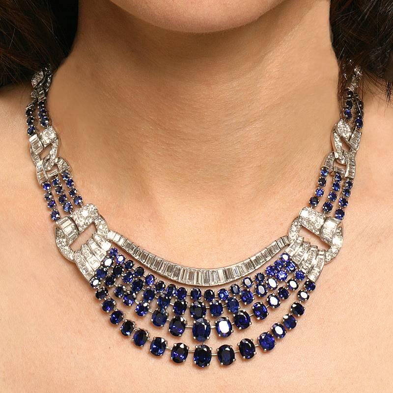 This gorgeous mid-century sapphire and diamond necklace unites playful motifs with serious gems. Its rich deep blue sapphires, draping softly across the neckline under their own weight, alternate with bold diamond buckles and curly volutes (referred