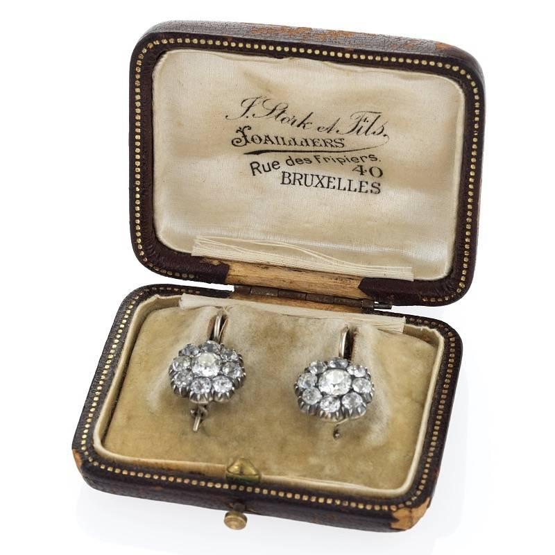 A pair of Antique silver top 14 karat gold cluster earrings with diamonds. The classic cluster earrings have 18 old mine cut diamonds with an approximate total weight of 3.90 carats, (including the .75 carat centers). With antique box. Wire backs