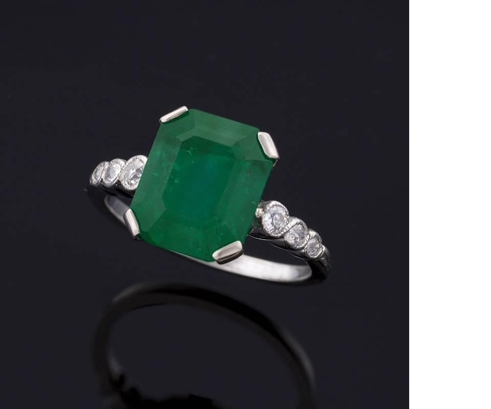 An Art Deco platinum, emerald and diamond ring. The center features a rectangular cut Colombian emerald that weighs 4.07 carats, flanked with 6 round old European-cut diamonds with an approximate total weight of .16 carats. The emerald has an