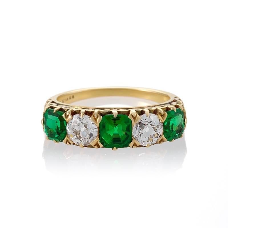 An Antique gold ring with diamonds and emeralds by T. B. Starr. The classic 5 stone ring has two old mine-cut diamonds with an approximate total weight of .65 carats, and three cushion-cut emeralds with an approximate total weight of .85 carats. The