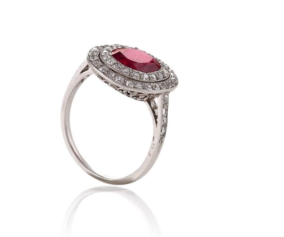 This early Art Deco platinum ring features a stunning cushion-cut Burmese unheated ruby, framed by a double halo of fiery old mine-cut diamonds. All the elements of this jewel—the vivid and rare, glowing ruby, set amidst concentric circles of