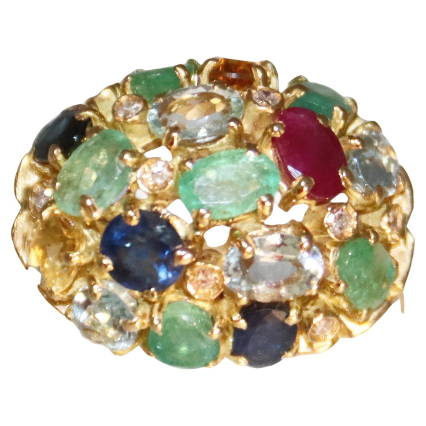 Questo anello in oro giallo 18 carati è audace e lussuoso.  ornato da un vivace assortimento di pietre preziose. Presenta zaffiri, smeraldi, rubini e acquamarine di taglio ovale, per un peso complessivo di 7,94 carati. Le pietre colorate sono