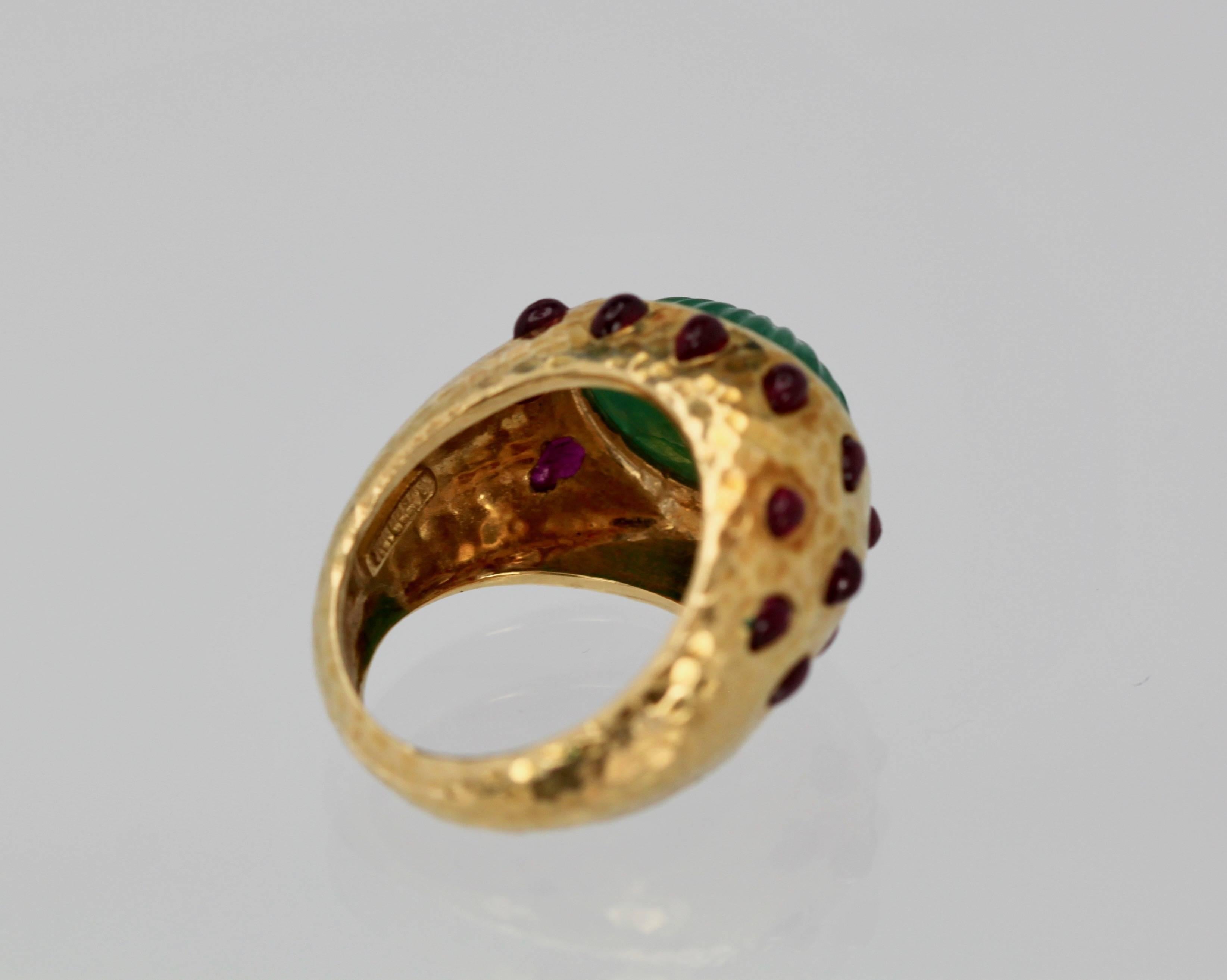 This ring is by no other than David Webb.  It has a hammered Yellow Gold finish with a Carved Emerald of approximately 8 carats and Ruby Cabochons ( 13) decorate the sides.  The ring is 15.03 mm across and 11.24 mm wide.  It weights 14.9 grams and