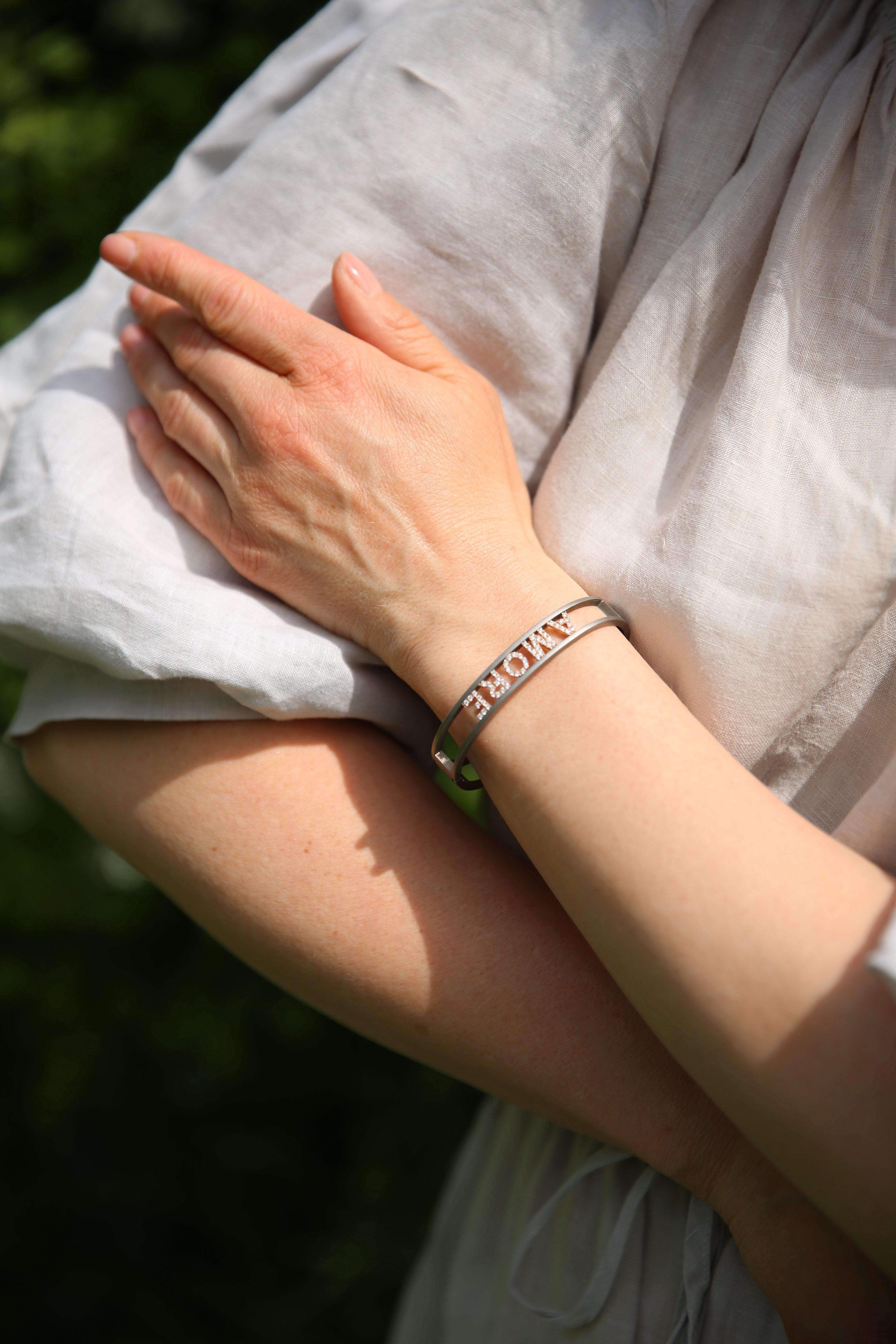 Un bracciale dal design contemporaneo firmato Anteo, sapientemente realizzato in titanio spazzolato e con incastonatura in oro 18kt.  con la parola 