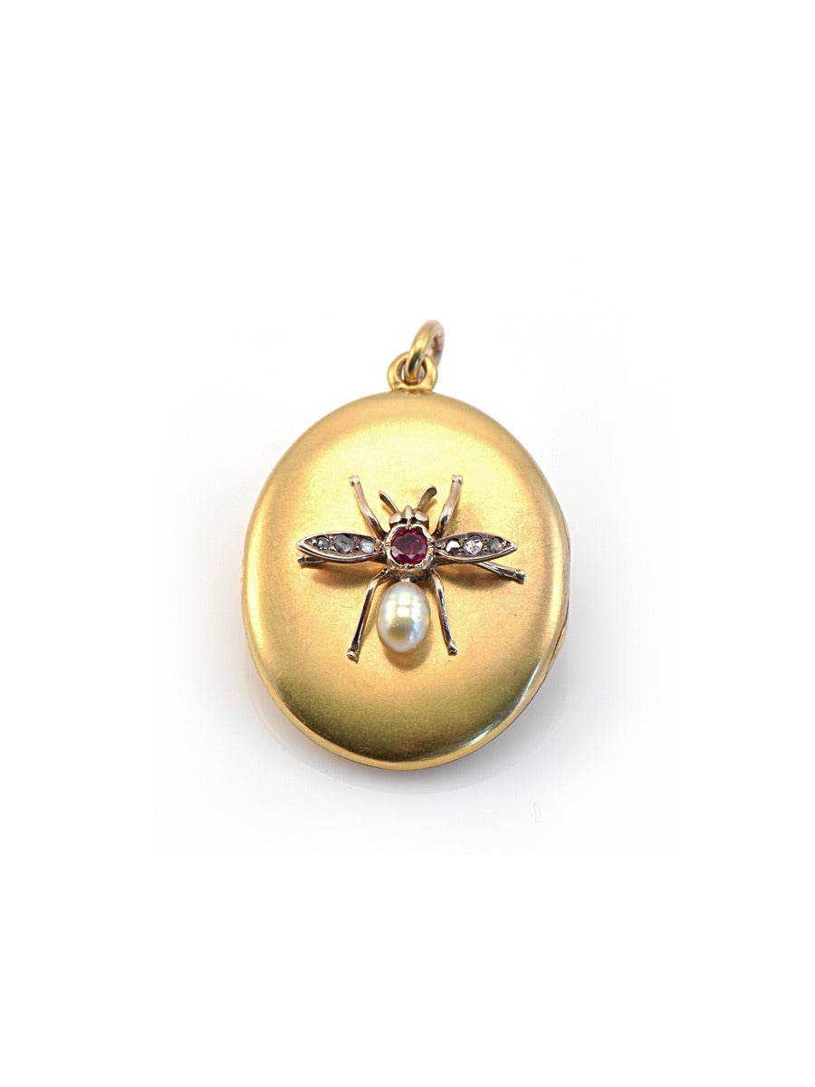 A charming golden locket with a honey bee, which sets a natural ruby, rosecut diamonds, and a golden pearl in 15k.