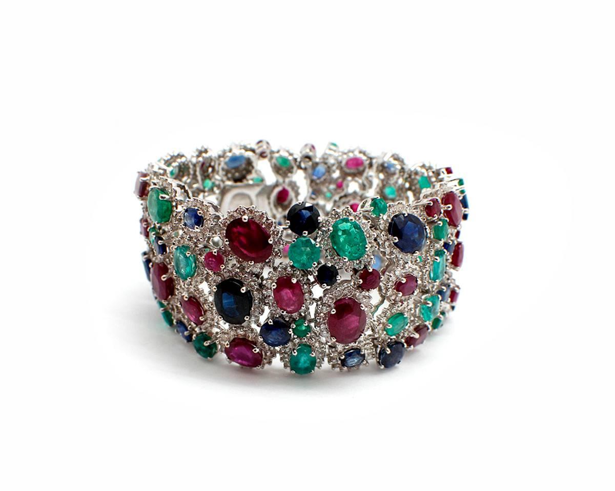 This stunning bracelet is made in 18k white gold. It holds various sizes of oval-cut rubies, emeralds, and sapphires. All the gemstones are accented by smaller round brilliant diamonds. The gemstones have a total weight of 83 carats, and the