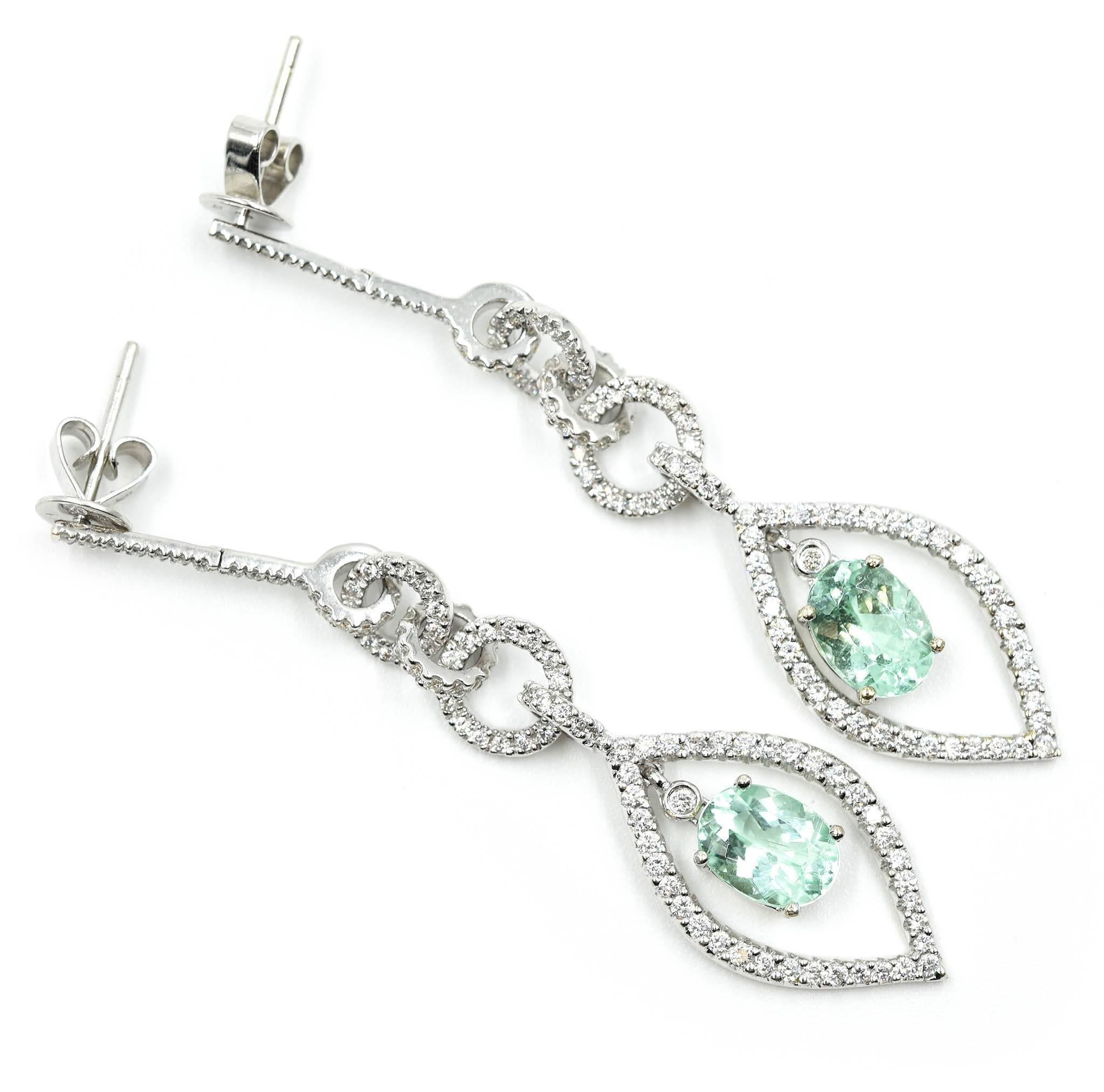 This pair of earrings is made in 18k white gold. Each earring features one oval-cut Mozambique Paraiba tourmaline that is accented by round diamonds. The tourmalines have a total weight of 2.64 carats, and the diamonds have an additional weight of