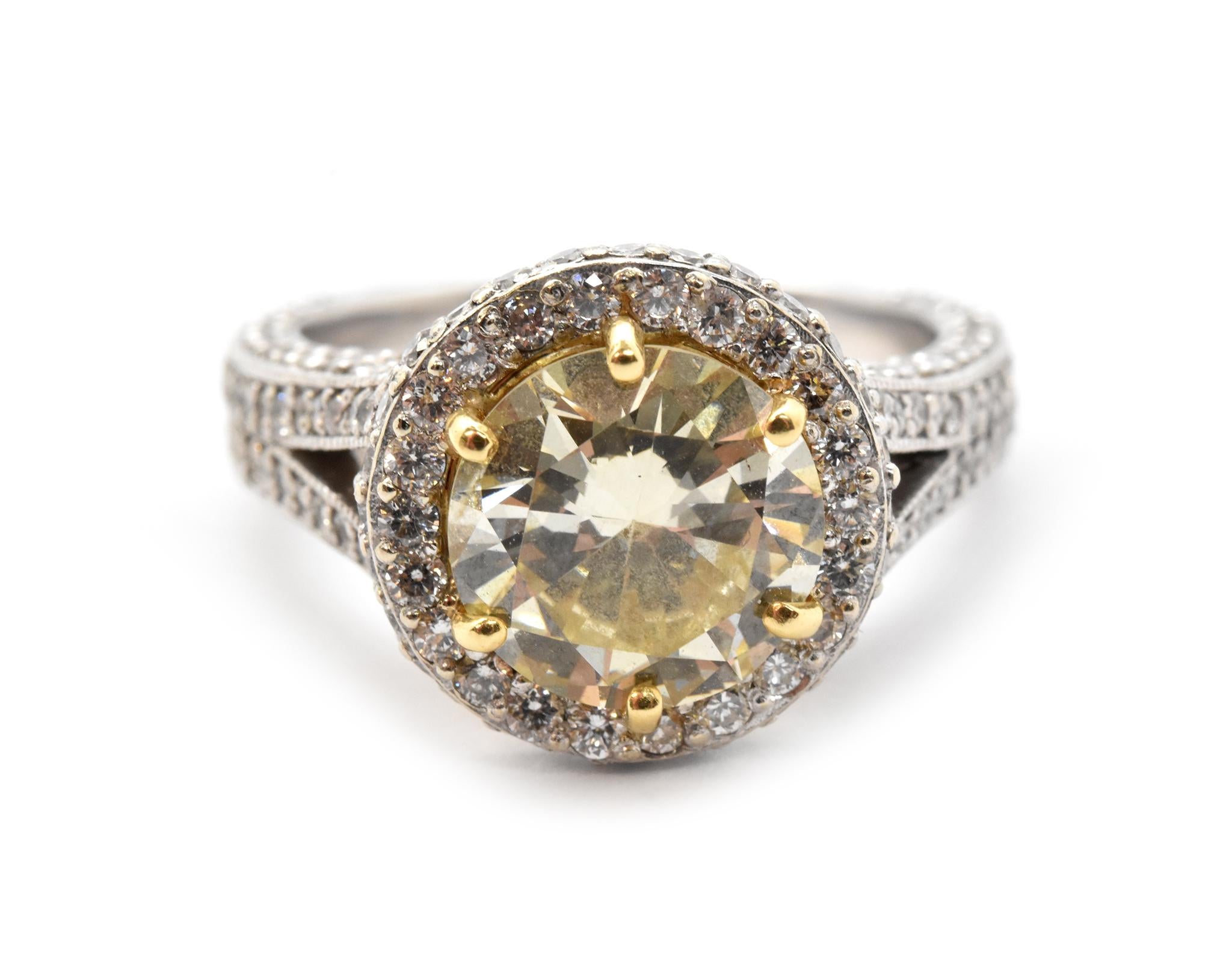 Shown in the picture is a jaw-dropping engagement ring designed with both 18k white and yellow gold, set into the mounting is a round brilliant 2.84ct fancy yellow diamond with a clarity of SI2. The mounting on the ring splits off on the shoulder,