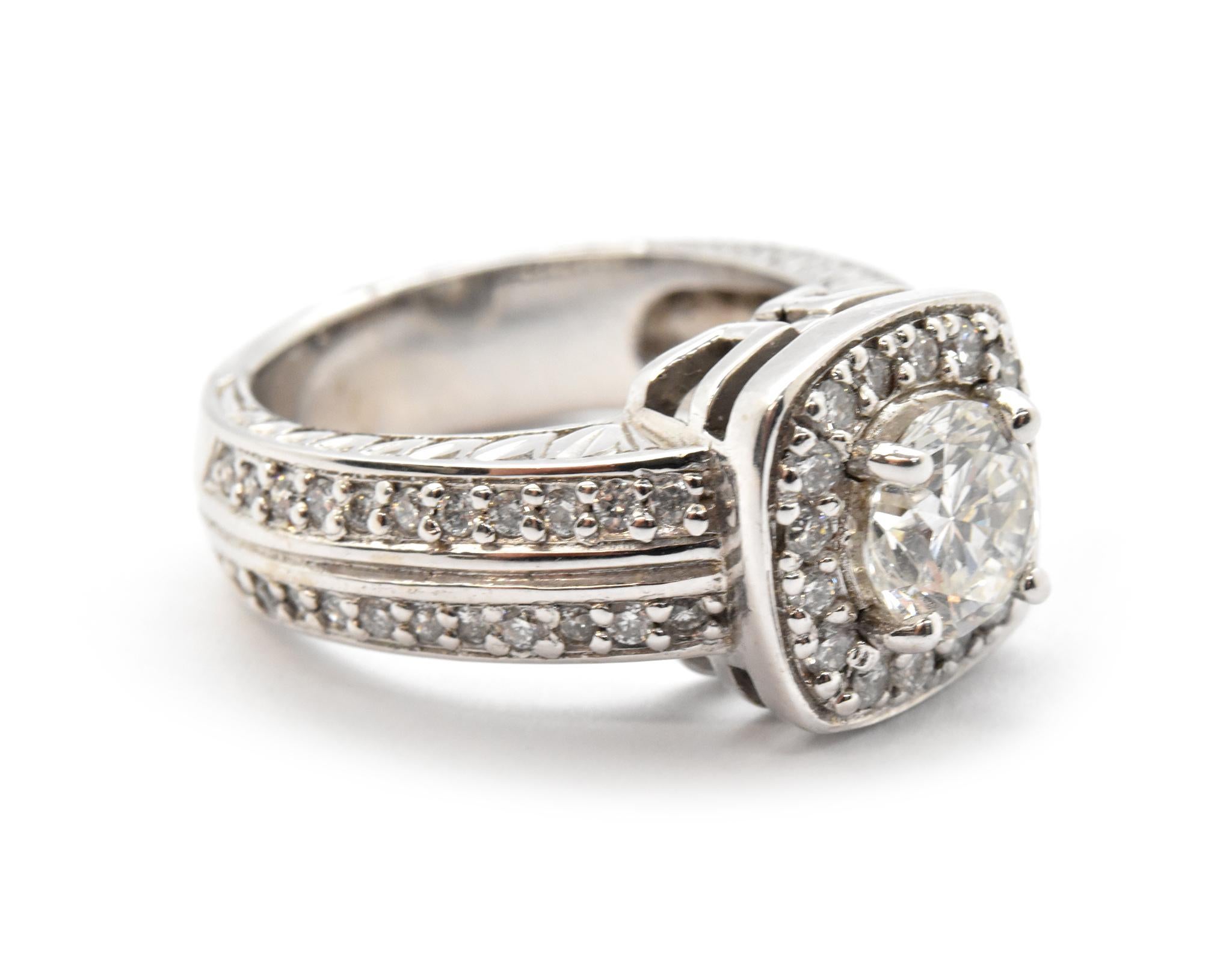 This ring is made in 14k white gold. It holds a 0.78-carat round brilliant diamond that is graded F in color and VS1 in clarity. The center stone is surrounded by a bezel of smaller round diamonds that extend down the shank. The additional stones