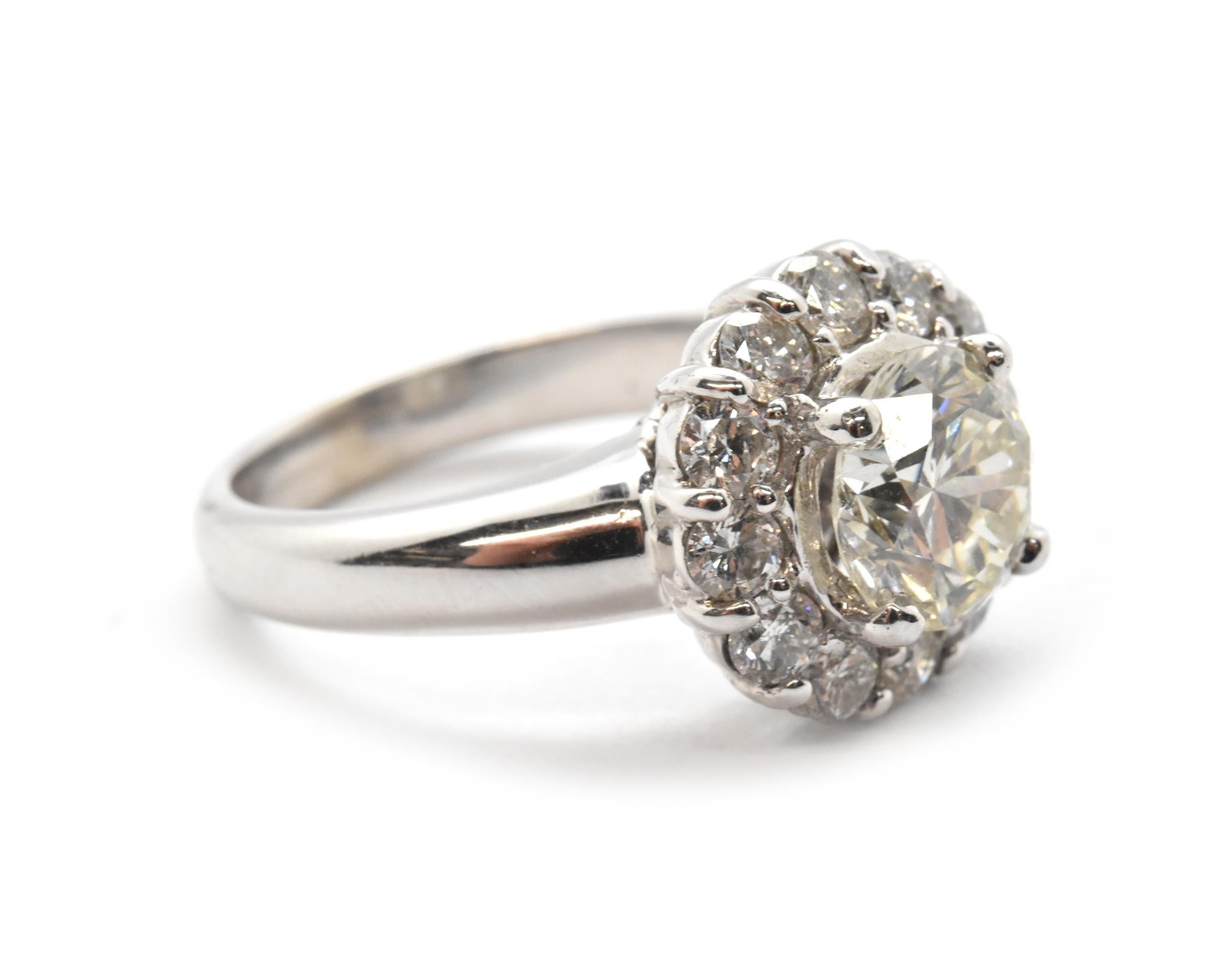 This gorgeous ring features a 1.76ct round brilliant diamond set into the center of a diamond halo. The center diamond is graded L in color and VS1 in clarity. The halo diamonds have an additional weight of 0.99cttw. The ring measures 13mm wide, and