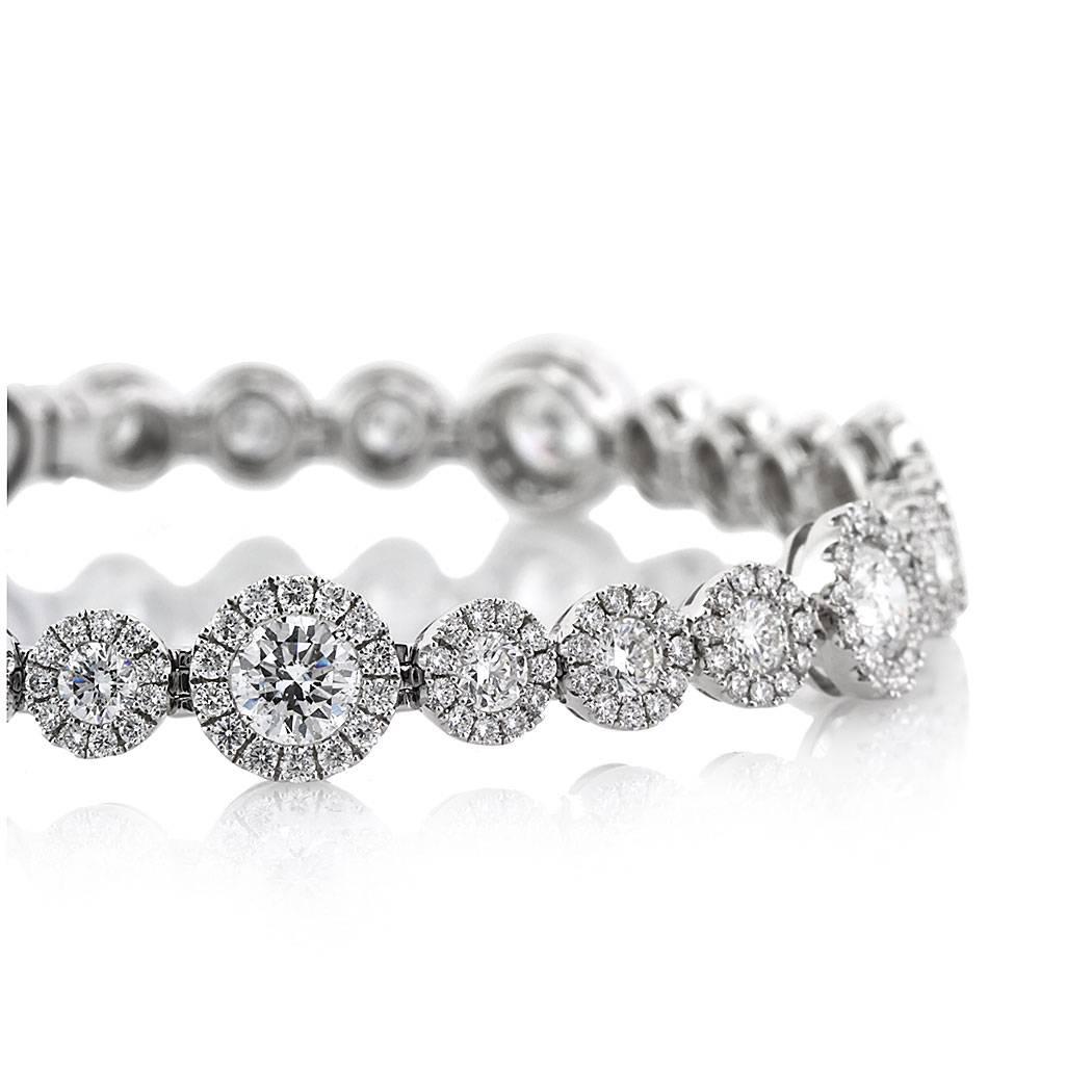 Handcrafted in 14k white gold, this exquisite diamond bracelet is set with 7.75ct of round brilliant cut diamonds graded at E-F, VS2-SI1. It showcases larger round brilliant cut diamonds at the center each surrounded by a delicate halo of smaller