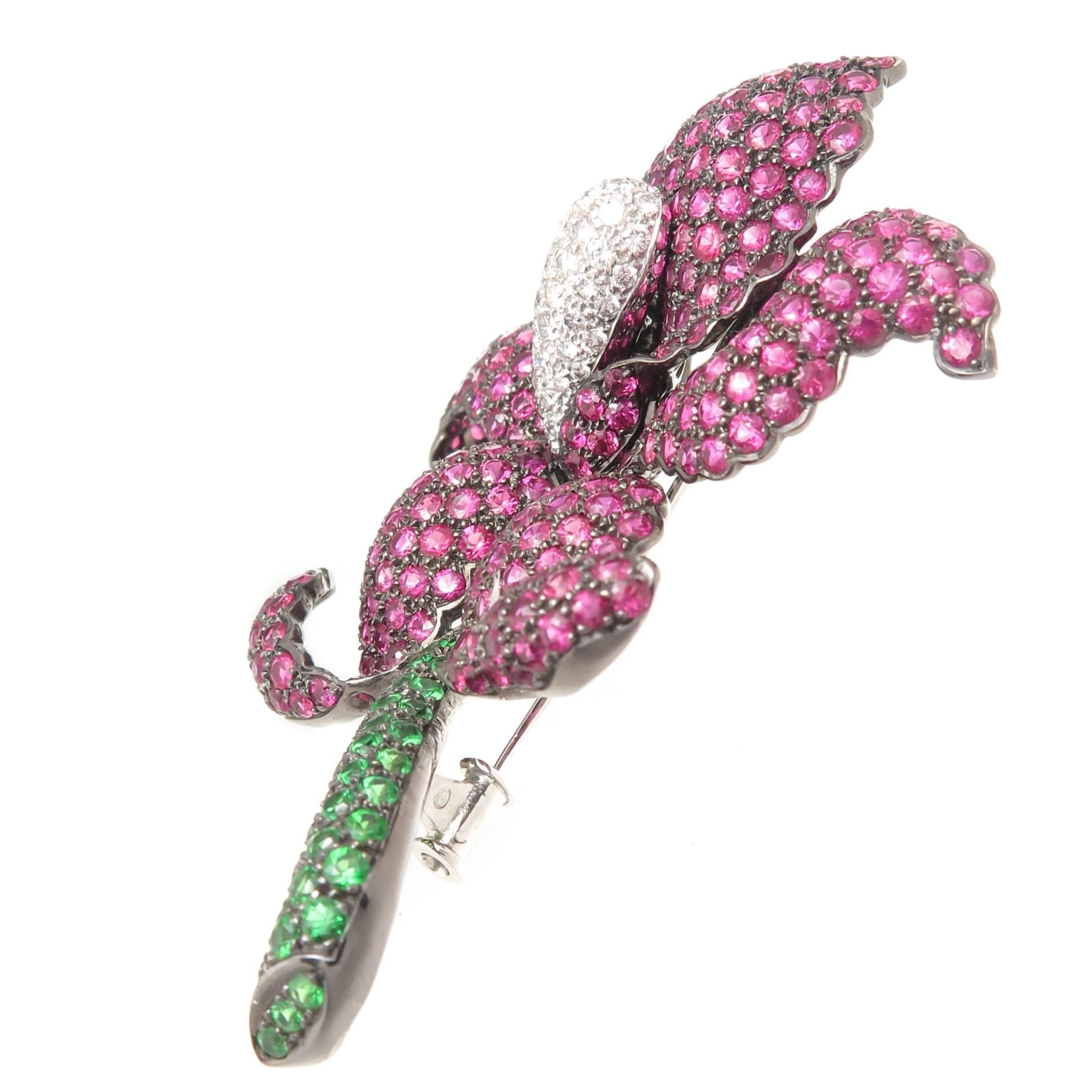 Circa 2010 18K Dark rhodium finished Gold Orchid Flower Brooch, measuring 2 3/4 inch in length and 2 inch wide. Set with Round Brilliant cut Rubies of fine bright color and totaling approximately 10 Carats, a stem of fine color Green Tsavorite