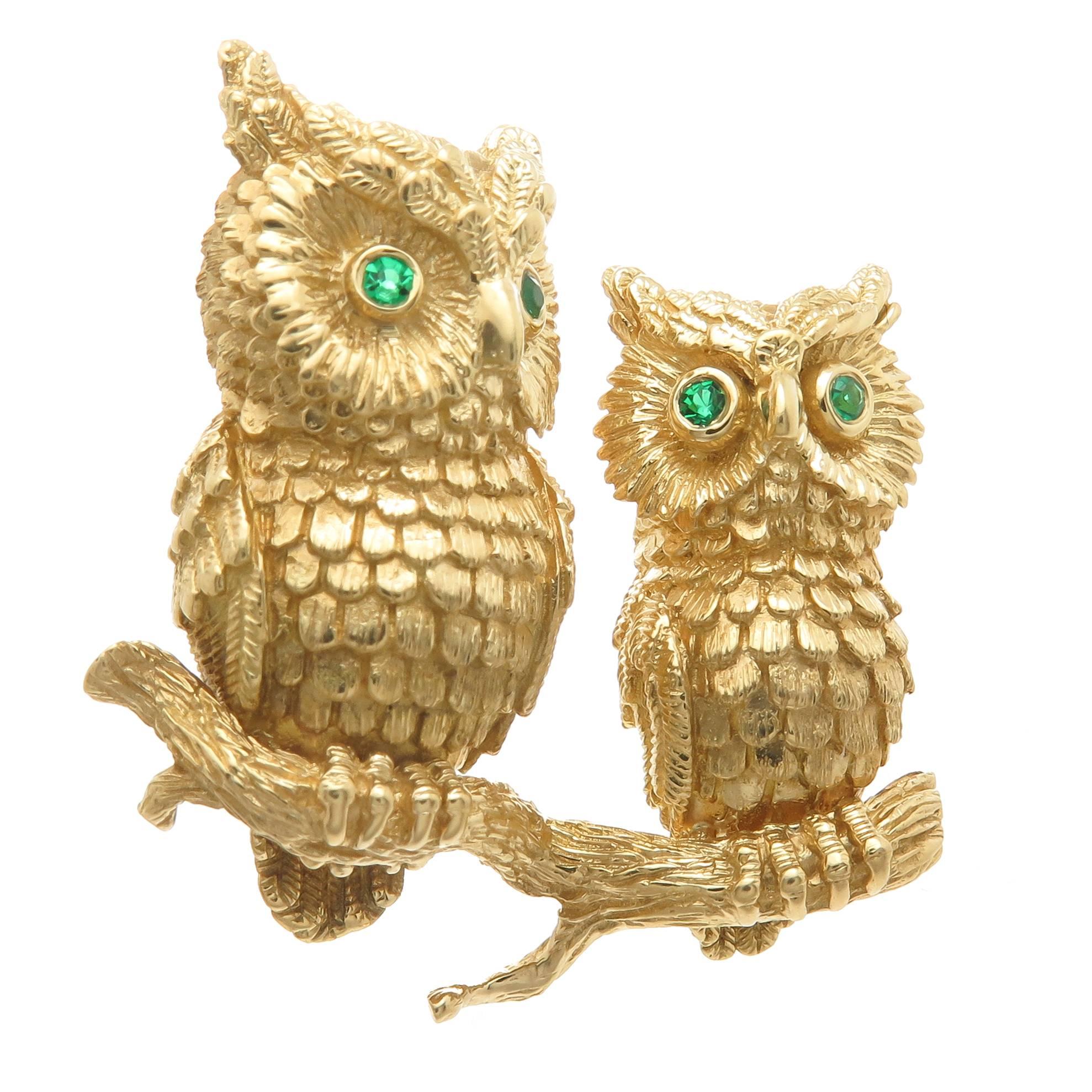 Circa 1990 Kurt Wayne 18K Yellow Gold Double Owls perched on a Branch Brooch, finely textured and detailed the Owls have Emerald set Eyes. Measuring 1 3/8 inch in length and 1 3/8 inch in height. 