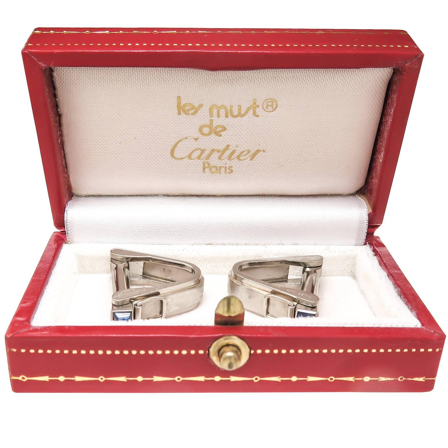 Circa 1990 Cartier 18K White Gold Stirrup form Cufflinks. Having a light brushed finish center and set with Cabochon Sapphires. Signed, numbered and in a Cartier presentation box.