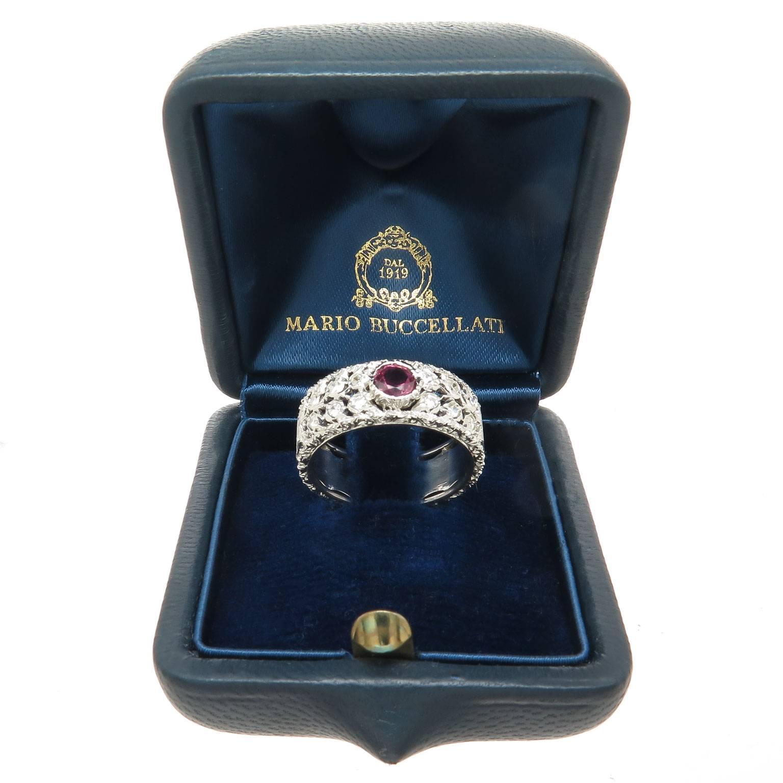 Mario Buccellati 18K White Gold Band Ring measuring 7 MM wide and set with Diamonds and a very Fine Color Ruby being approximately 1/2 Carat, further decorated in the famous Buccellati hand engraved fashion. Finger size = 7. Comes in the Original