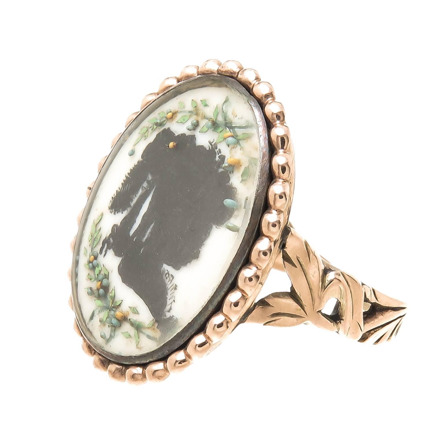 Circa 1850 Yellow Gold Mourning Ring possibly English with a miniature hand painted silhouette of a Young Girl, further decorated with wreaths of colored cut steel and enamel under Glass. The top measures 7/8 X 1/2 inch. Finger size = 7.