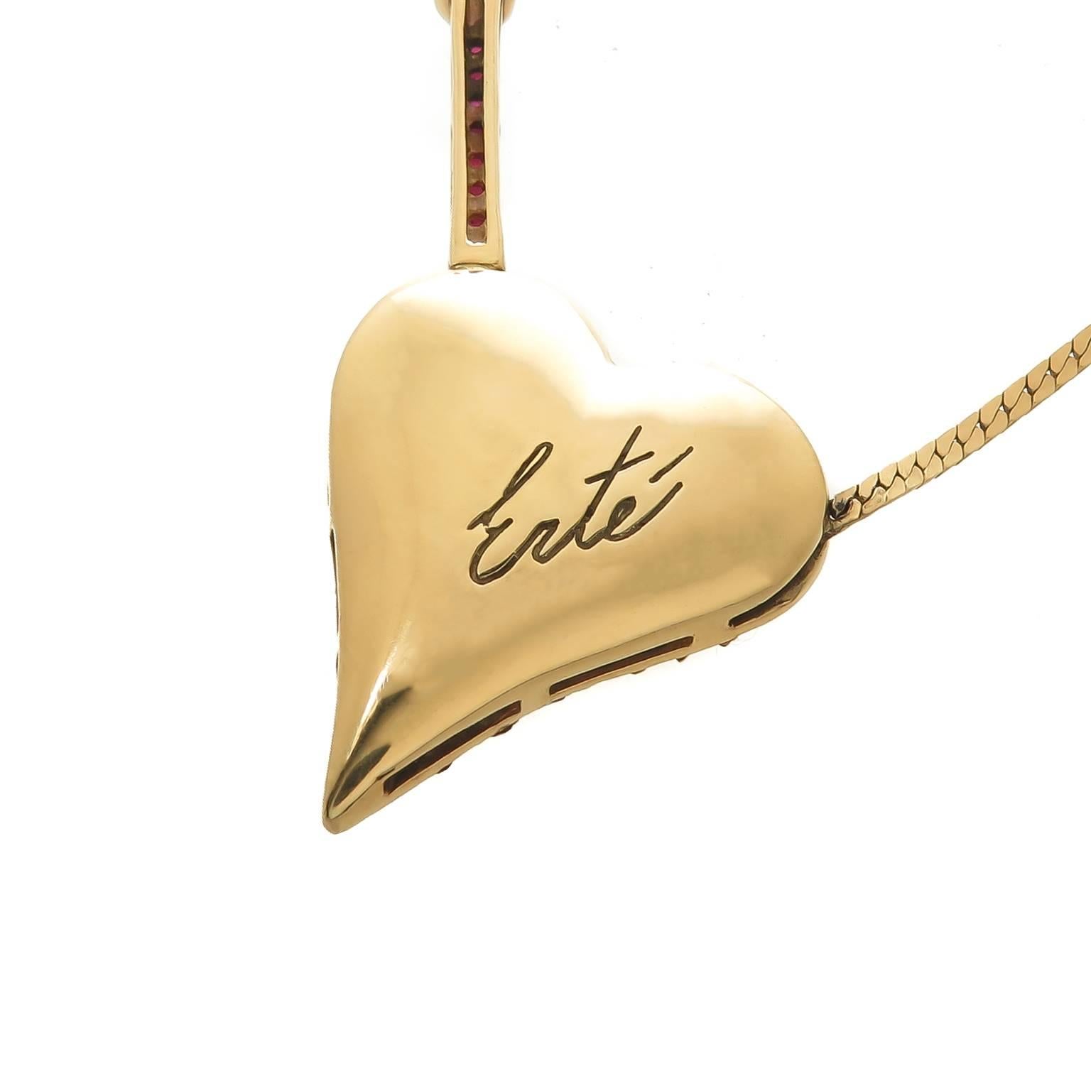 Circa 1980s Erte Beauty of the Beast 14K yellow Gold necklace. The heart measures 1 1/8 inch, 2 inch in length with the arrow. Set with Round Brilliant cut Diamonds and fine color Rubies. Suspended from an 18 1/2 inch chain. Signed and numbered and
