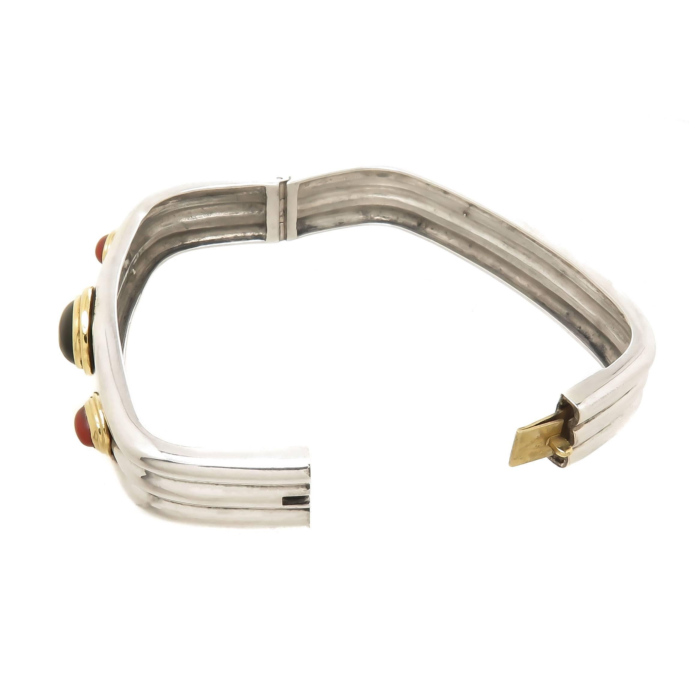Circa 1970s Cartier Sterling Silver Bangle Bracelet, measuring 3/8 inch wide and having a ribbed design, 18K Yellow Gold bezel set Corals and Onyx. Inside measurement 6 1/2 inch.
