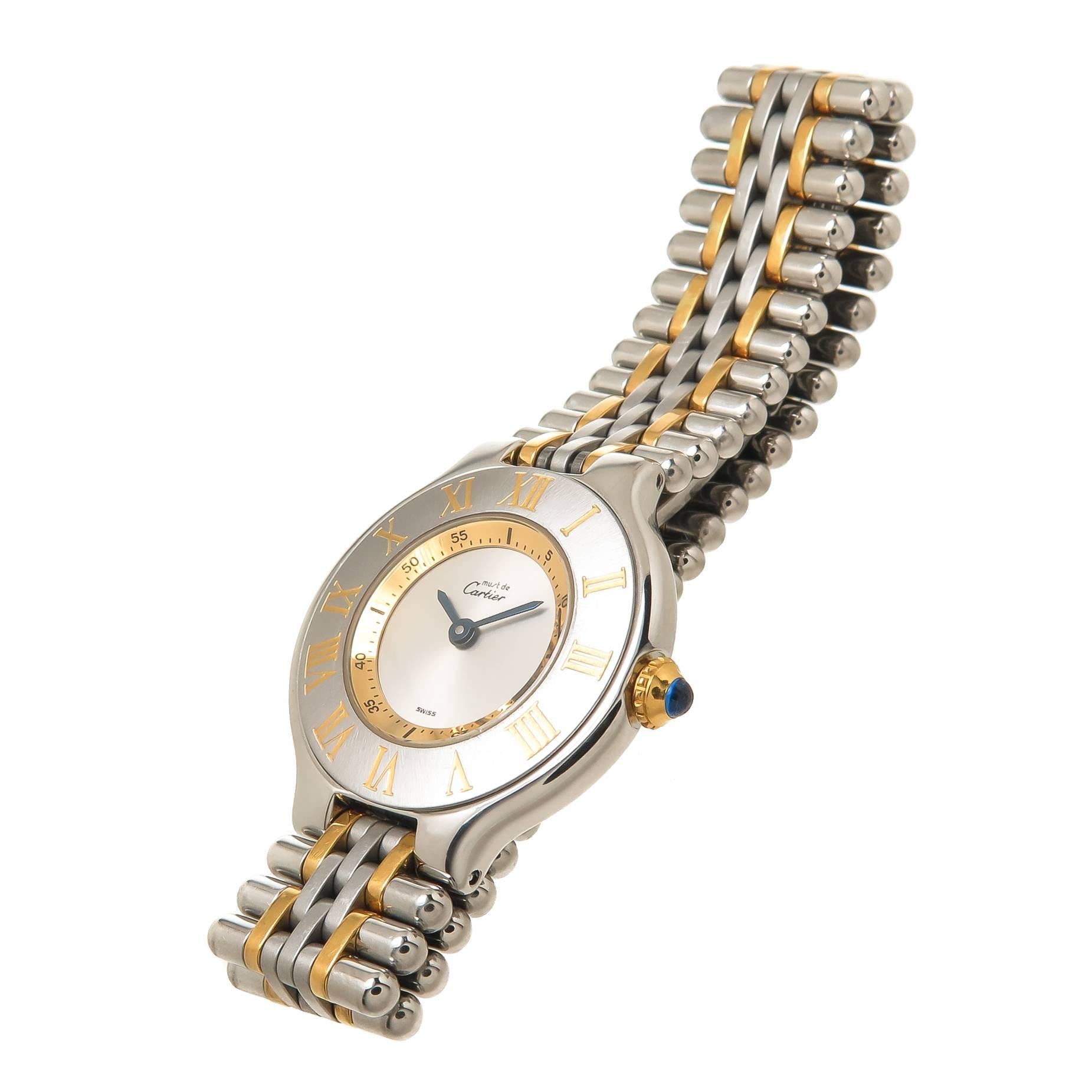 Circa 1990s Cartier, Must De Cartier 21 Ladies Wrist watch, 28 MM Stainless Steel with Gold accents case and a Gold crown set with a sapphire. Quartz Movement, Silver Dial. 9/16 inch wide Steel and Gold link bracelet with Deployment clasp. Total